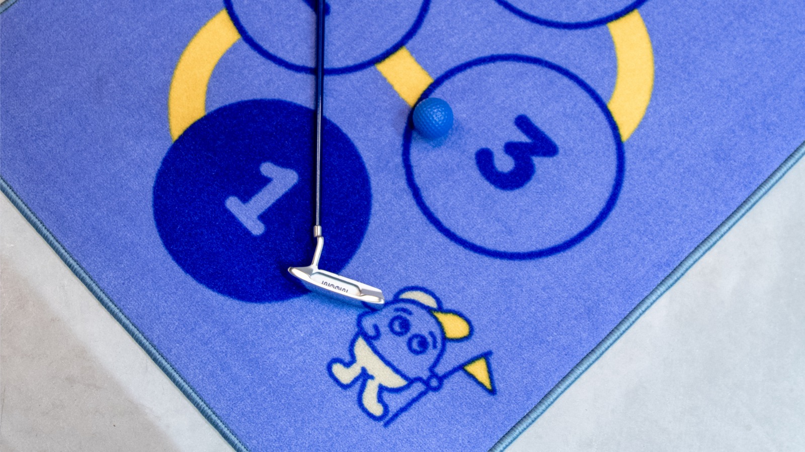 A young child playing golf at home on a WOOW Golf putting mat with a parent watching